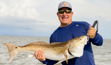 Man holding a fish wearing Vapor Apparel shirt, hat, and shorts